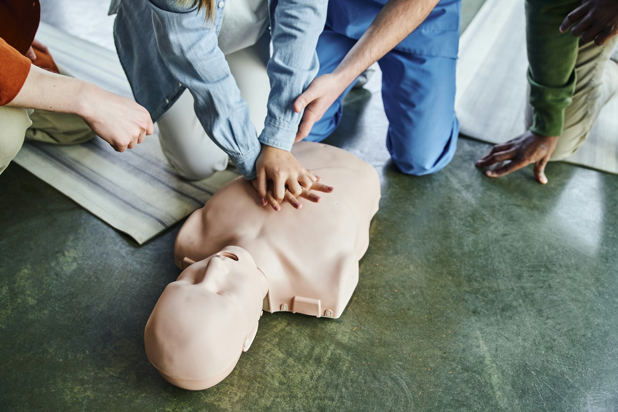 cropped view of paramedic assisting young woman practicing chest compressions on CPR manikin