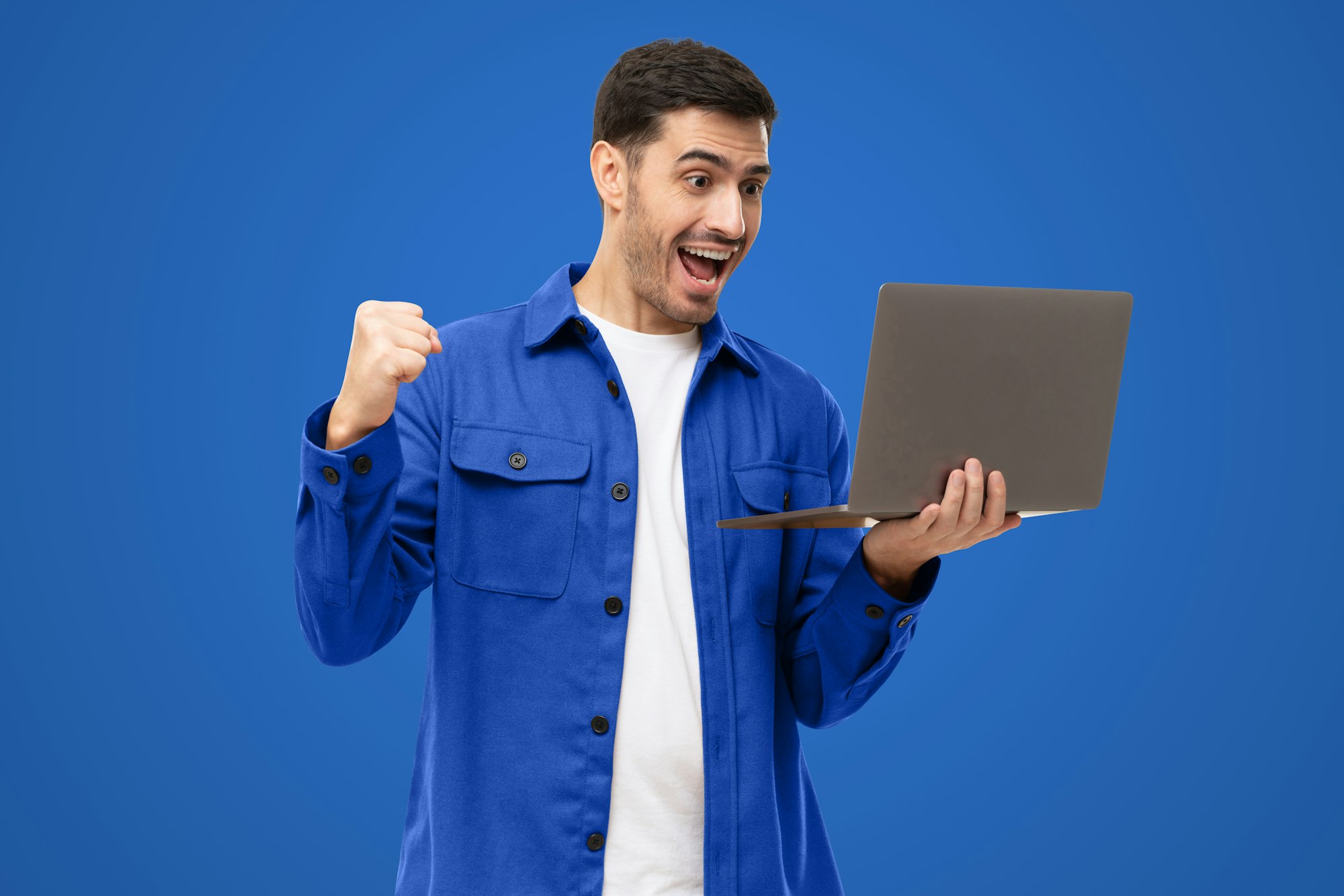 Excited sucessful modern business man holding laptop and raising arm up to celebrate achievement