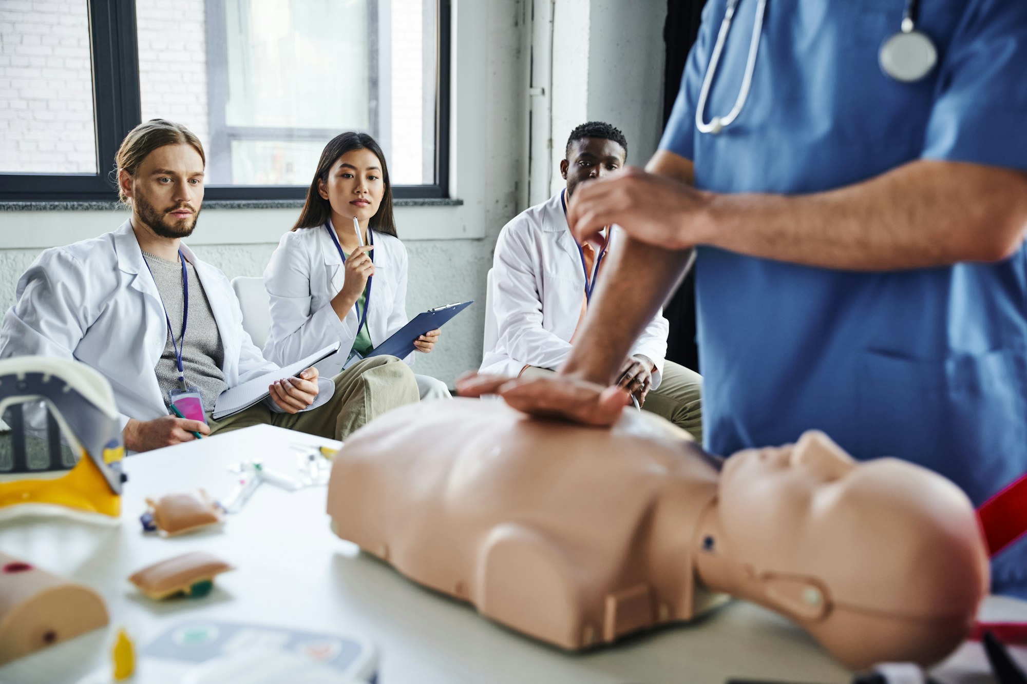 young multiethnic students in white coats looking at paramedic showing life-saving techniques