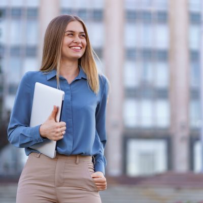 Blonde young woman smiling portrait wearing blue gentle shirt over building background